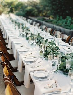 a long table is set with white plates and silverware