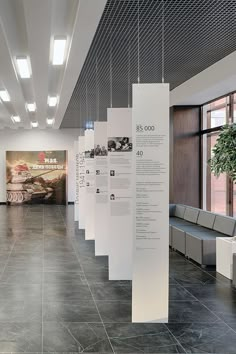 an office lobby with white walls and black tile flooring that has information about cars hanging from the ceiling