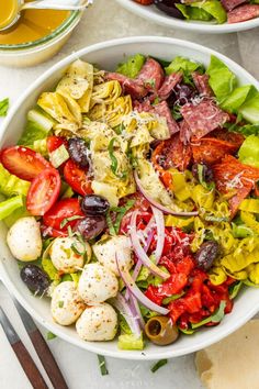 two white bowls filled with salad on top of a table next to utensils