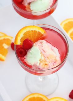 two glasses filled with ice cream, orange slices and raspberries on a white tray