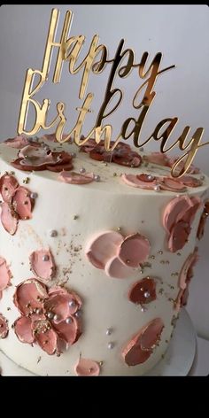 a white cake with pink frosting and gold foil flowers on it's top