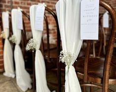 the chairs are lined up with white flowers and place cards on them for guests to sign