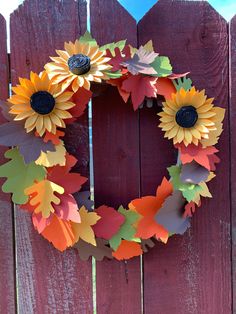 a wooden fence with a wreath made out of paper leaves and sunflowers on it