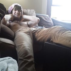 a shirtless man sitting on a couch with his feet up in the air and smiling