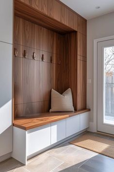 a wooden bench sitting under a window next to a white door with hooks on it