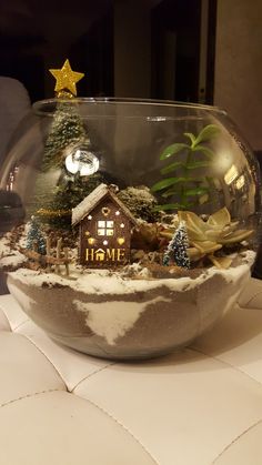 a glass bowl filled with snow covered plants and a small house in the center surrounded by trees