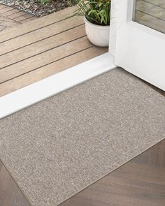 a door mat on the outside of a house with a potted plant next to it