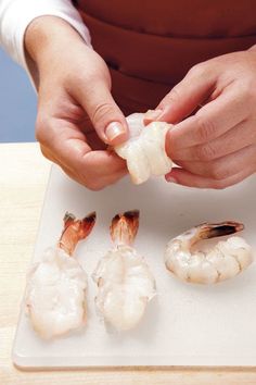 a person is peeling shrimp on a cutting board with other pieces in front of them