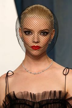 a woman in a black dress with a veil over her head and red lips on the runway