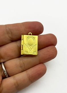 a hand holding a gold colored square shaped pendant