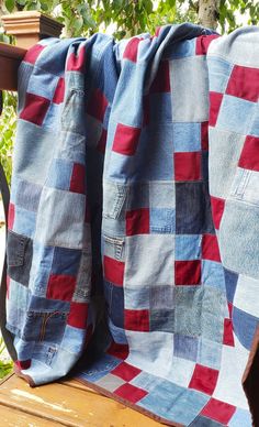 a blue and red blanket sitting on top of a wooden bench next to a tree