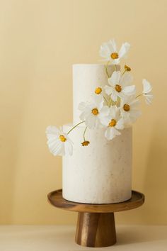 there is a white cake with flowers on the top and bottom tier, sitting on a wooden stand