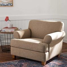 a tan chair sitting on top of a wooden floor next to a table with flowers