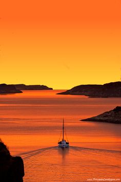 a boat is out on the water at sunset or sunrise, as seen from a cliff