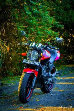 a red and black motorcycle parked on the side of a road next to some trees