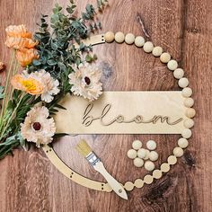 a wooden sign that says bloom next to some flowers and paintbrush on a table