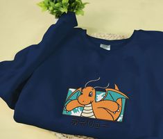 Introducing our Dragonite Embroidered Sweatshirt, the perfect gift for Christmas, birthdays, or any holiday celebration! Made with meticulous embroidery, this sweater showcases the majestic Dragonite in all its glory. The soft and cozy fabric ensures comfort while keeping you warm during the chilly winter months. With its vibrant colors and intricate design, this sweater is [...] Long Sleeve Fleece Top With Embroidered Graphics, Blue Long Sleeve Top As Gift, Blue Long Sleeve Top For Gift, Blue Long Sleeve Top As A Gift, Embroidered Logo Sweatshirt As A Gift, Winter Long Sleeve T-shirt With Embroidered Text, Embroidered Logo Long Sleeve Sweatshirt, Long Sleeve Sweatshirt With Embroidered Logo Gift, Blue Long Sleeve T-shirt For Gift