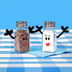 two salt and pepper shakers with faces drawn on them sitting on a tablecloth