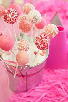 pink and white cake pops are in a bucket on the table with other desserts