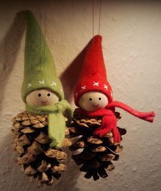 two little gnomes are hanging from pine cones on the wall, one is wearing a green and red hat