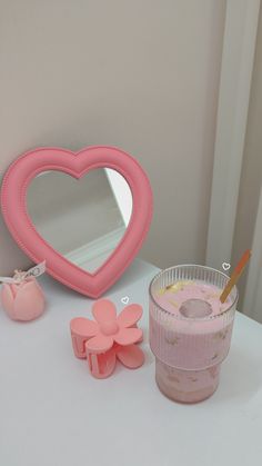 a pink heart shaped mirror next to a cup and cookie cutters on a table