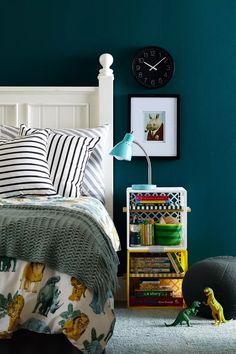 a bedroom with green walls and white headboard, bookshelf, toy dinosaur on the floor