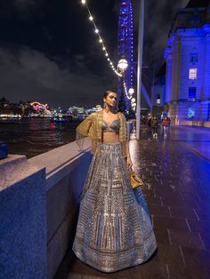 This lehenga set features antique silver sequin embroidery in a geometric pattern. The blouse shows crystal tassels at the waist. Embroidered dupatta also shows crystal tassels. The outfit can be paired with (an optional) antique gold cape jacket with matching embroidery. The jacket has heavy beaded tassels.From Seema Gujral's For the love of London collection. DELIVERY TIMEPlease allow 8-12 weeks for your outfit to arrive. FABRIC DETAILSNet Professional cleaning only. Sequin Lehenga, Matching Embroidery, Cape Jacket, Sequin Embroidery, Embroidered Dupatta, Sequins Embroidery, Wedding Outfits, 12 Weeks, Silver Sequin