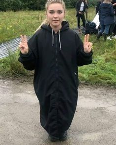 a girl in a black raincoat is making the peace sign with her hands while standing on a path