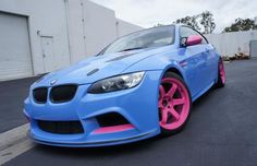 a blue car with pink rims parked in front of a building