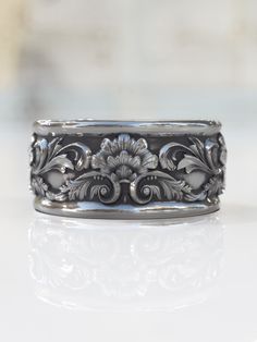 a silver ring with flowers and leaves on the inside, sitting on a white surface