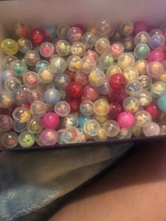 a box filled with lots of different colored plastic balls on top of a table next to a woman's stomach