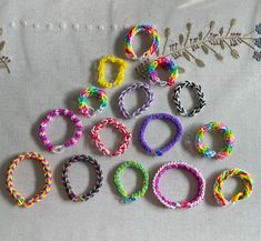 many different colored bracelets are arranged on a white tablecloth next to an embroidered plant