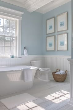 a white bathroom with blue walls and pictures on the wall above the bathtub, along with a wicker basket