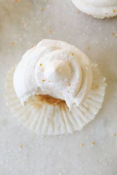 three cupcakes with white frosting and sprinkles on them sitting on a table