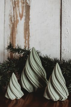 three small white vases sitting on top of a wooden table next to evergreen branches