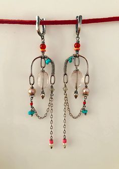 two pairs of dangling earrings with beads and chains hanging from the hooks on a red string