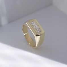 a yellow gold ring with two princess cut diamonds on the front and side, sitting on a white surface