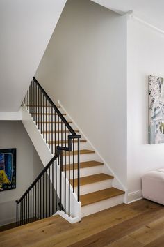 a living room with white walls and wooden flooring next to a staircase leading up to a bed