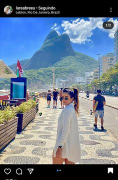 a woman standing on the side of a road next to a lush green mountain covered in clouds