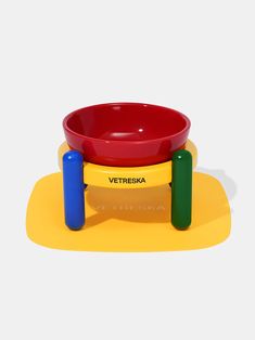 a red bowl sitting on top of a yellow and green stand with two blue legs