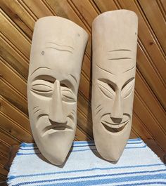 two clay masks sitting on top of a blue and white striped table cloth next to each other