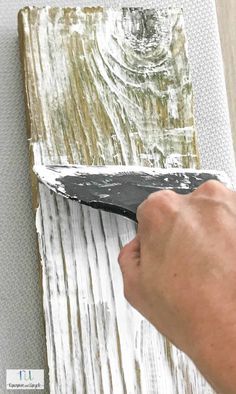 a person using a pair of scissors to cut wood planks with white paint on it