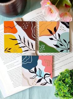 three colorful cards sitting on top of an open book next to a plant and potted plant