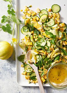 a white plate topped with cucumbers and corn next to a glass of dressing