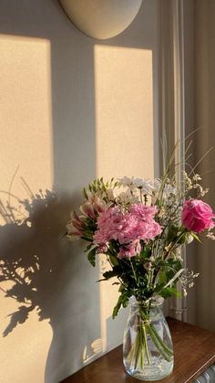 a vase filled with pink and white flowers sitting on top of a wooden table next to a window