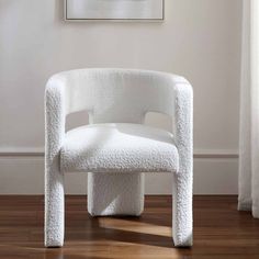 a white chair sitting on top of a hard wood floor next to a painting and window