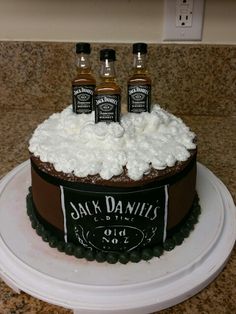 three bottles of jack daniels on top of a chocolate cake with whipped cream frosting