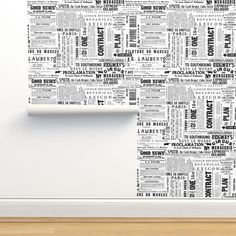 a white wall mounted to the side of a wooden floor next to a window with a black and white newspaper print on it