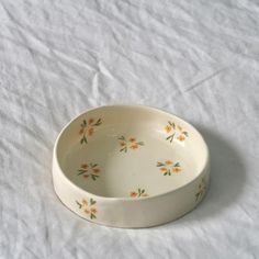 a white bowl with orange and green flowers on it sitting on a white tablecloth