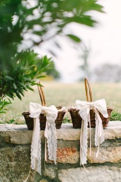 three wicker baskets with bows tied to them sitting on a stone wall next to a tree